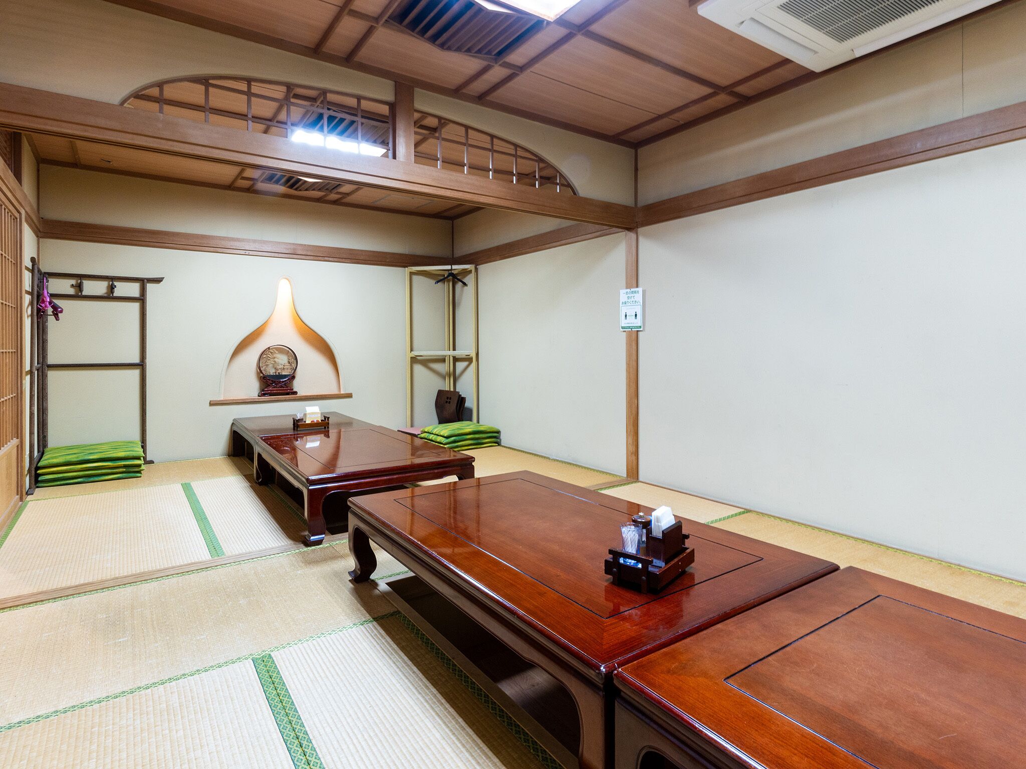A traditional Japanese-style room with tatami flooring, a low wooden table, a hanging lamp, and a shelf with a decorative item.