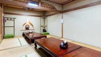 Quarto tradicional japonês com tatame, uma mesa de madeira baixa, um candeeiro pendente e uma prateleira com um objeto decorativo.