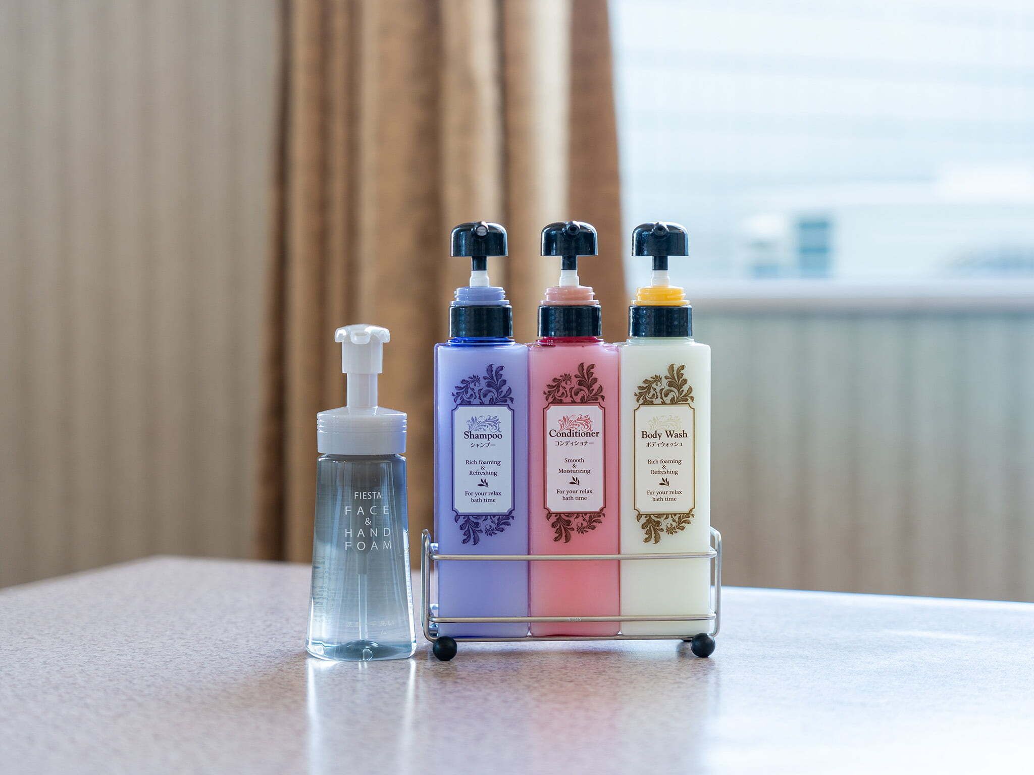 A bathroom with a hand soap dispenser, a shampoo bottle, a conditioner bottle, and a body wash bottle on a small cart.