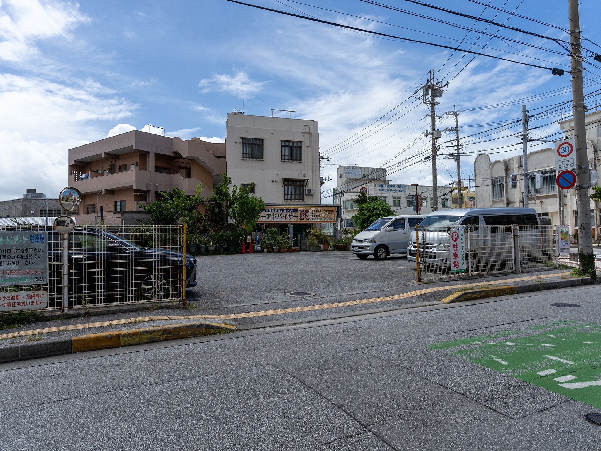 A street view with a building that has a sign for a business, a parked car, and a no parking sign.