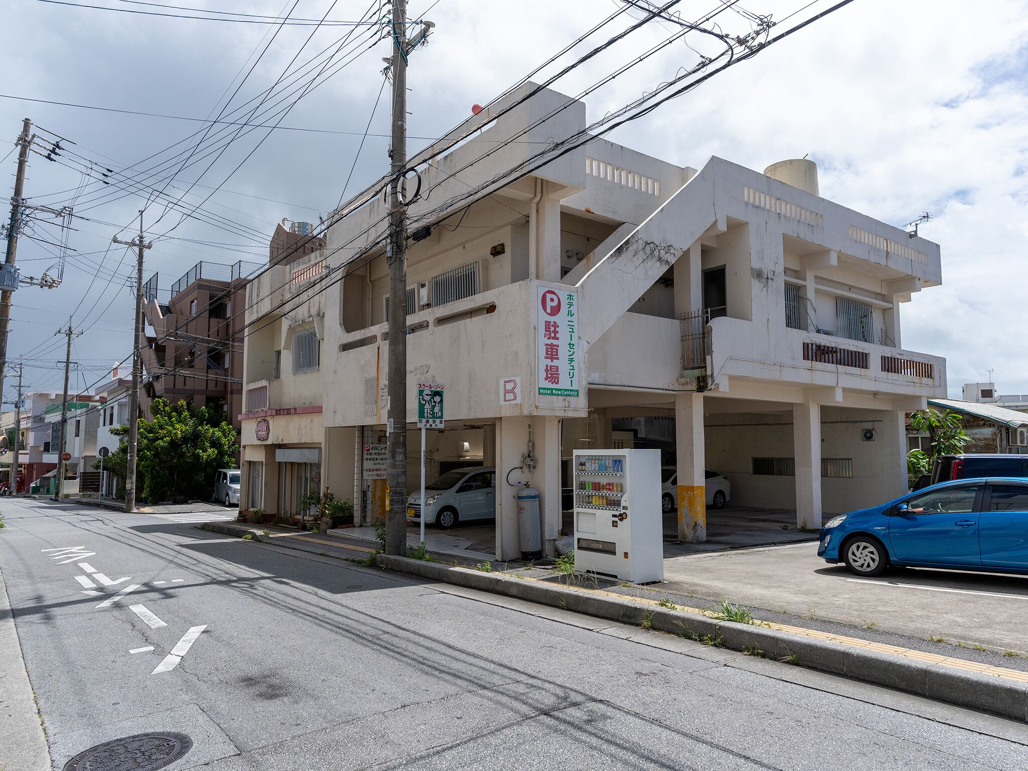 A multi-story building with a parking area, a vending machine, and a car parked in front.
