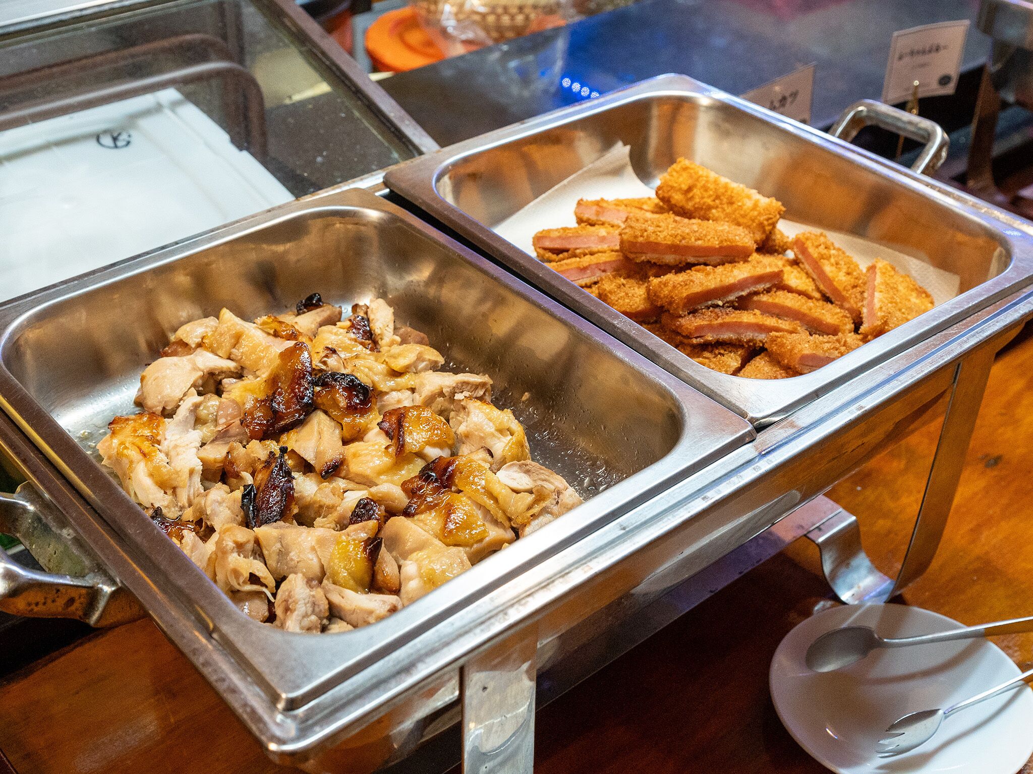 Un bufé con dos bandejas metálicas, una con carne en rodajas y la otra con tiras de pollo empanizado.
