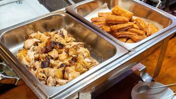 Un bufé con dos bandejas metálicas, una con carne en rodajas y la otra con tiras de pollo empanizado.
