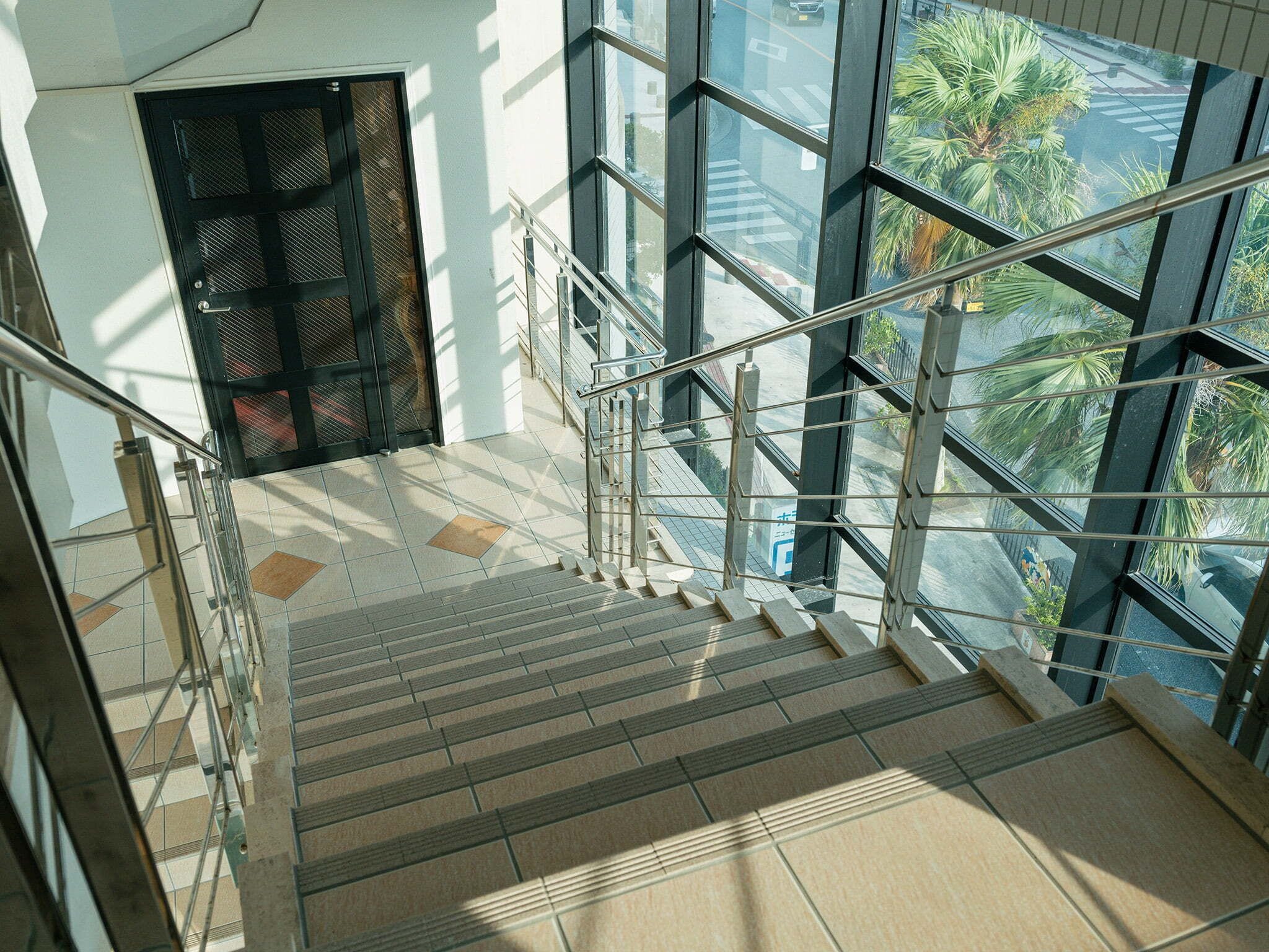 A modern staircase with glass railings and a view of palm trees outside.