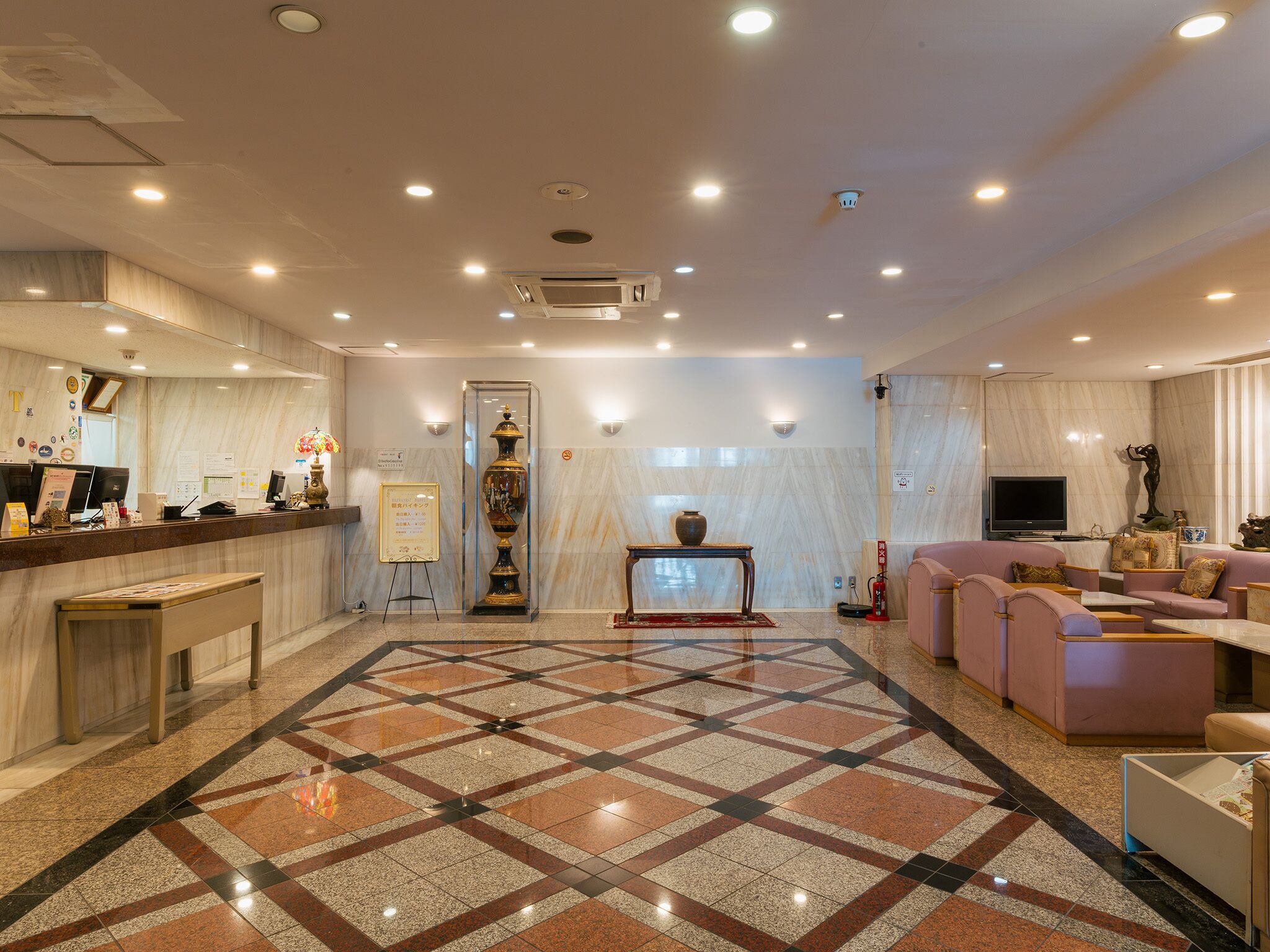 A hotel lobby with a reception desk, seating area, and a patterned floor.