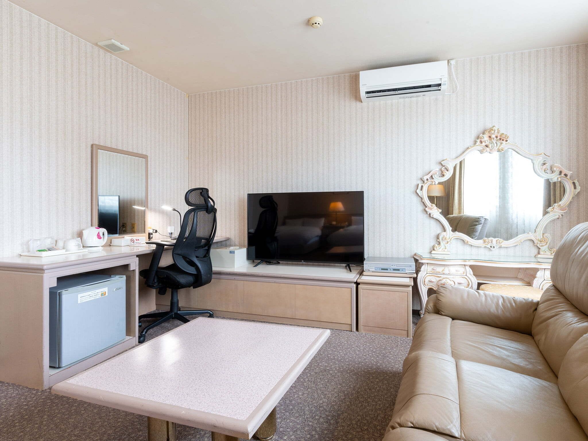 A hotel room with a desk, chair, television, sofa, and a decorative mirror.
