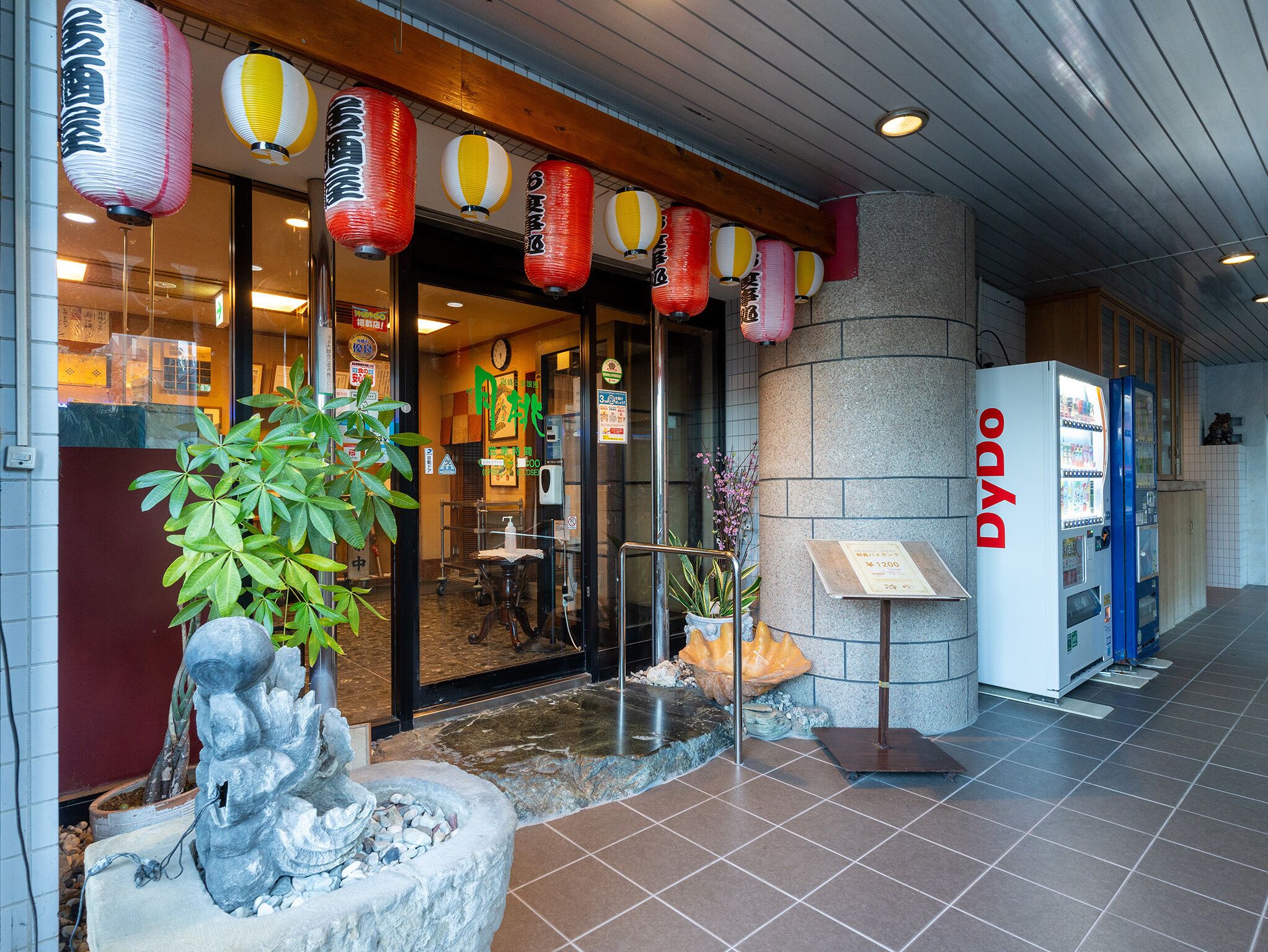 A hotel entrance with traditional lanterns, a reception desk, and a vending machine.
