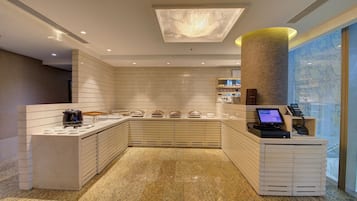 A modern hotel lobby with a reception desk, a coffee station, and a large window with a view.