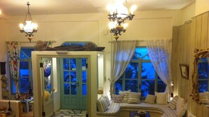 A cozy room with a stone-patterned floor, a green door, a sofa with striped cushions, and a wooden wall. - Afrodite Hotel (Tinos)