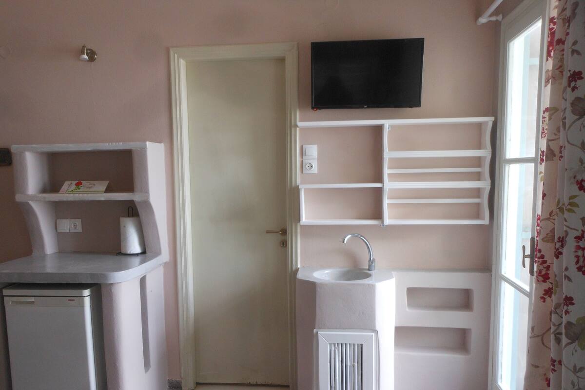 A compact kitchenette with a built-in dishwasher, a white sink, and a flat-screen TV mounted above the counter.