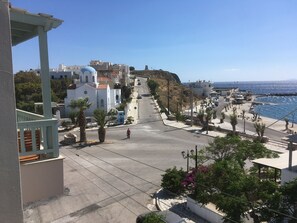 A coastal street with buildings, a clear sky, and a person walking. - Afrodite Hotel (Tinos)