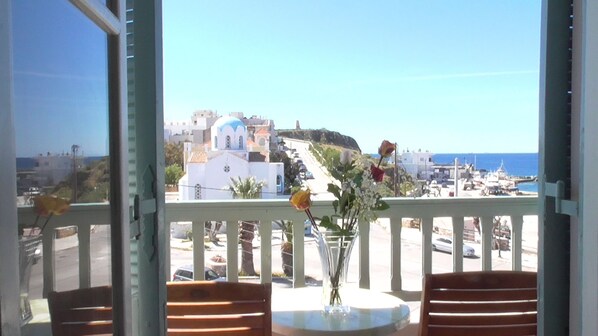 A balcony with a view of a coastal town, a vase with flowers, and wooden chairs. - Afrodite Hotel (Tinos)