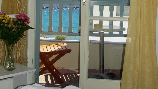 A room with a view of the sea, a wooden bench, a white towel, and a vase with flowers. - Afrodite Hotel (Tinos)