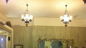 A room with a patterned floor, a sofa, a mirror, and two chandeliers. - Afrodite Hotel (Tinos)