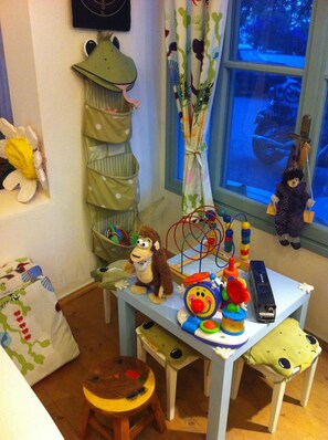 Uma área de recreação infantil com uma pequena mesa, brinquedos e um organizador pendurado em formato de sapo.