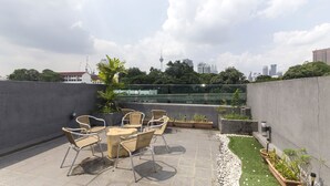 A rooftop terrace with a table and chairs, surrounded by greenery and a city skyline in the background. - i-Hotel Kuala Lumpur (Kuala Lumpur)