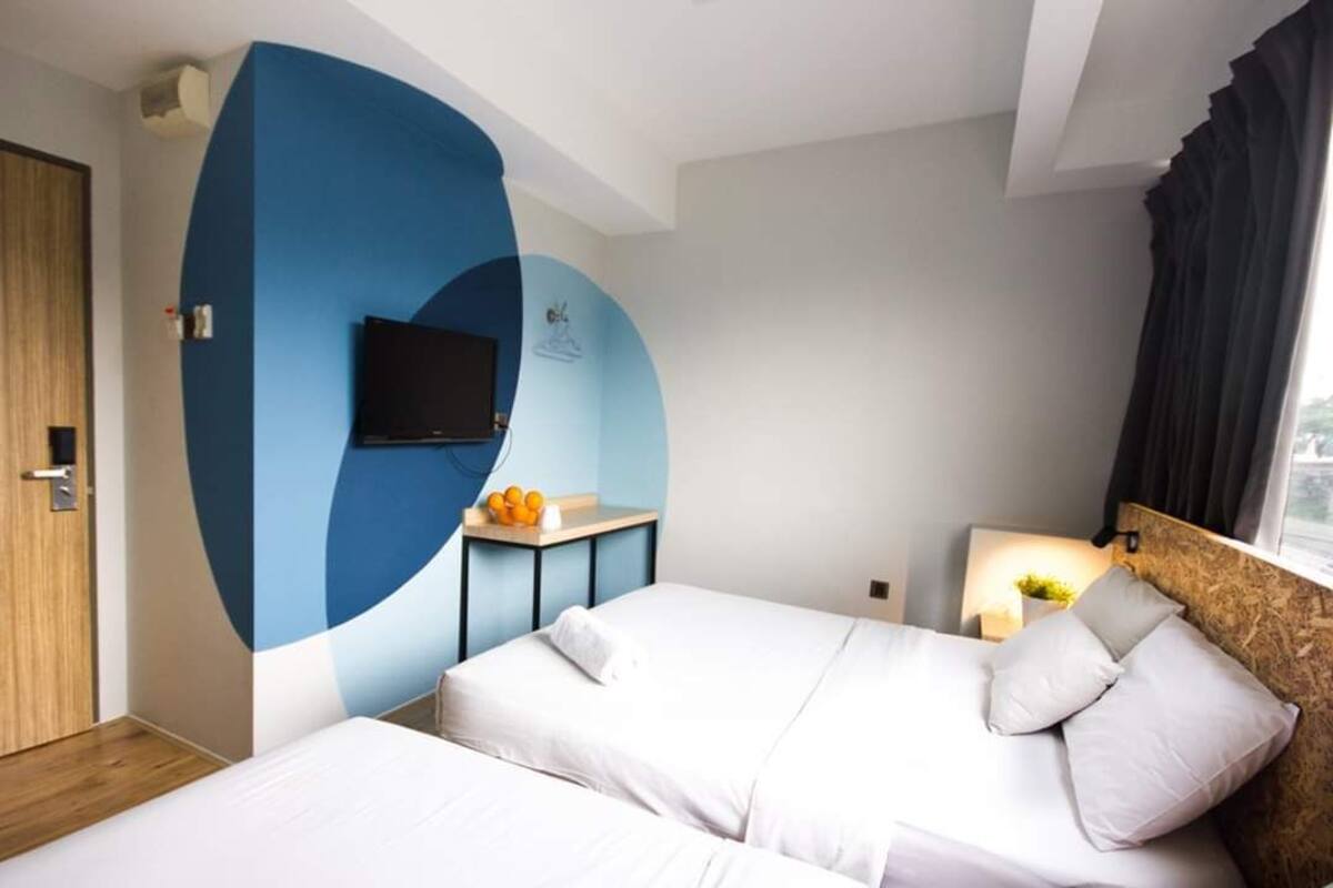 Habitación de hotel con dos camas, un televisor, una mesita con fruta y una ventana con cortinas.