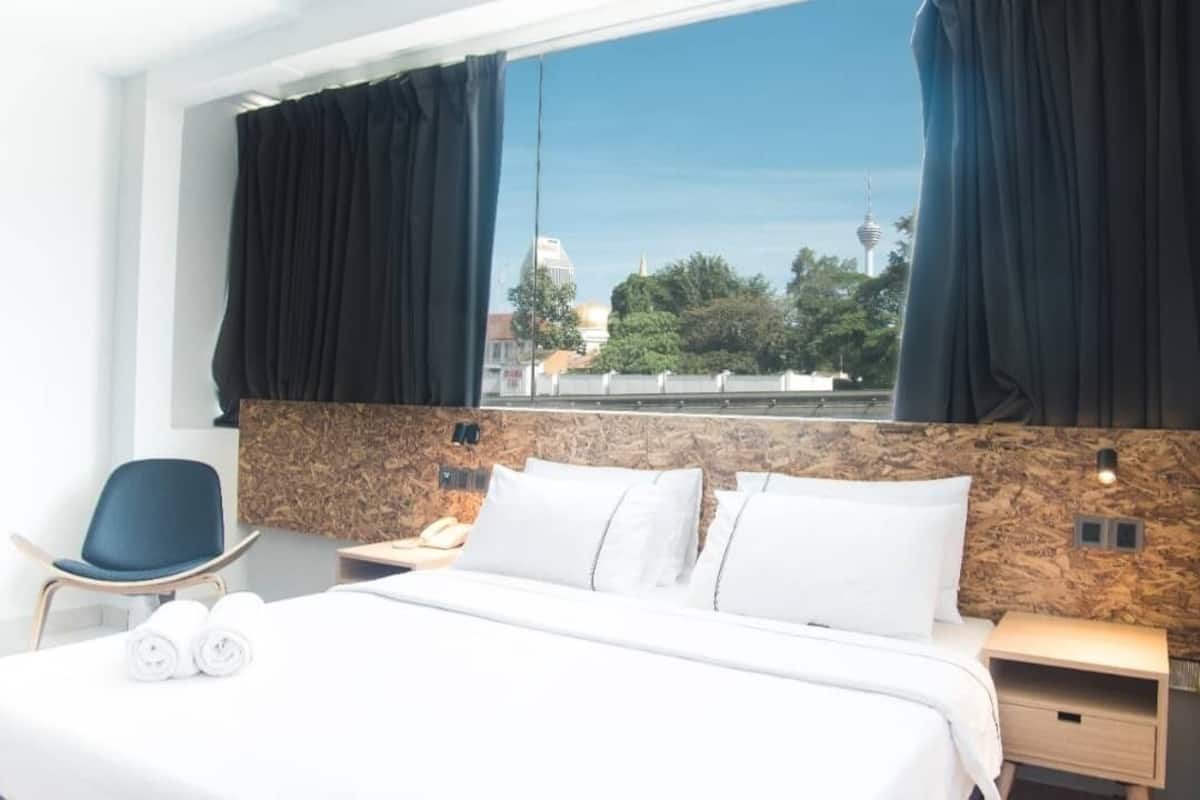Una habitación de hotel con cama, una silla, una mesita de noche y una ventana con cortinas.