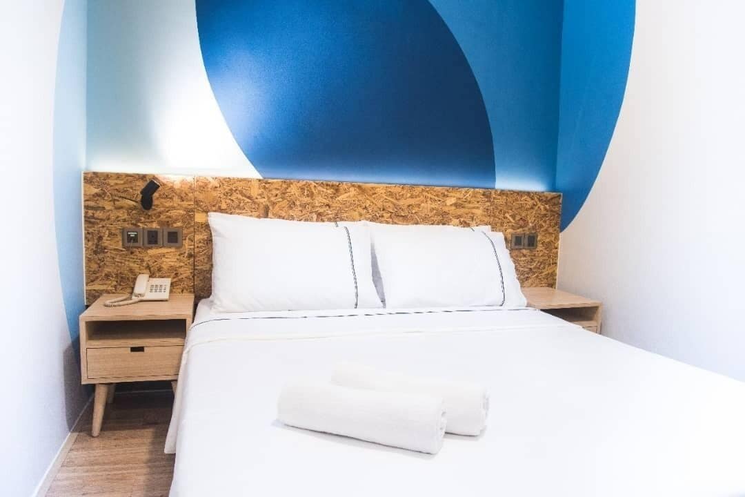 Une chambre d’hôtel avec un lit, une table de chevet, un téléphone et un mur orné d’un motif abstrait bleu.