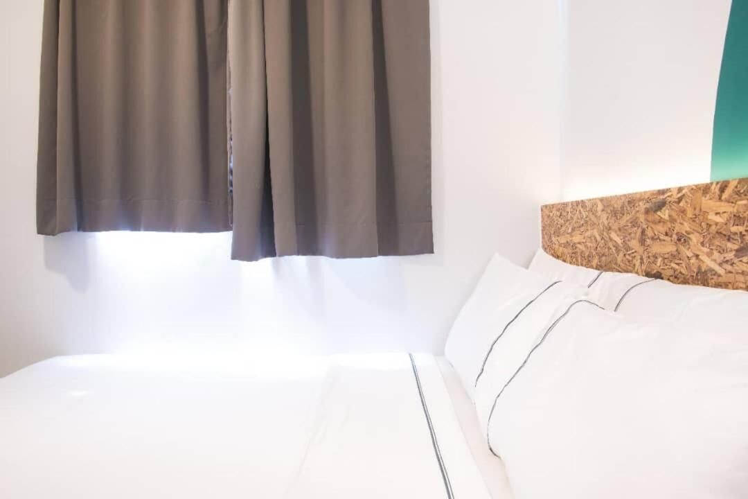 A hotel room with a bed, a headboard with a textured design, and a window with curtains.