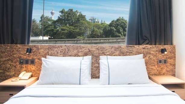 A hotel room with a bed, two bedside tables, a telephone, and a view of a tower and trees. - i-Hotel Kuala Lumpur (Kuala Lumpur)