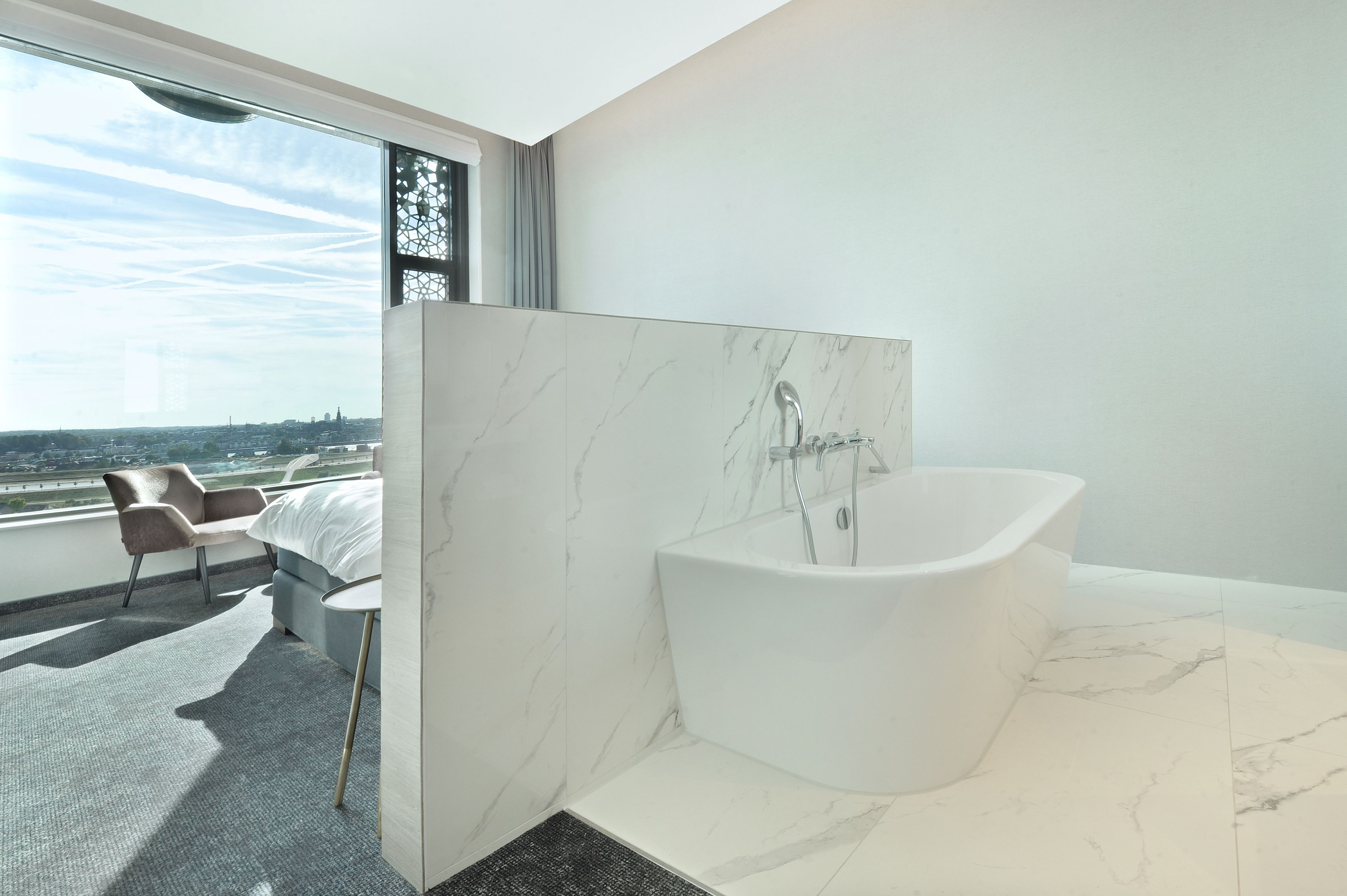 Un baño moderno con una bañera independiente, un ventanal con vistas a la ciudad y una zona de estar con una silla y una mesa.