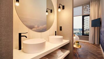 Un baño moderno con dos lavabos redondos, un espejo grande y vistas de la ciudad a través de un ventanal.