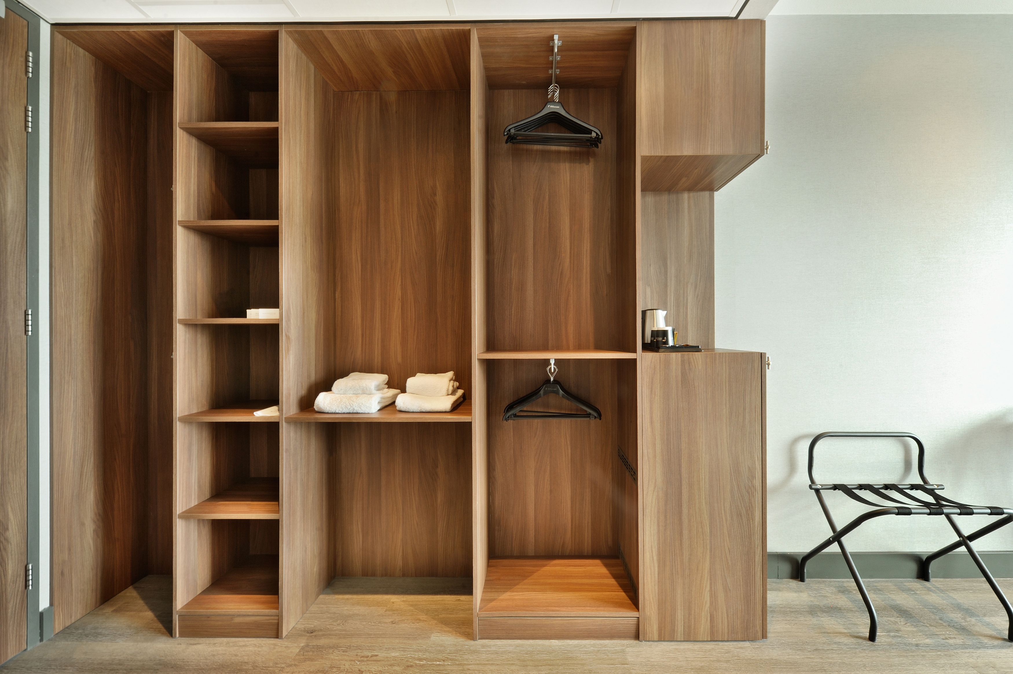 Une armoire en bois avec plusieurs étagères et un espace pour suspendre des vêtements, une petite table et une chaise.