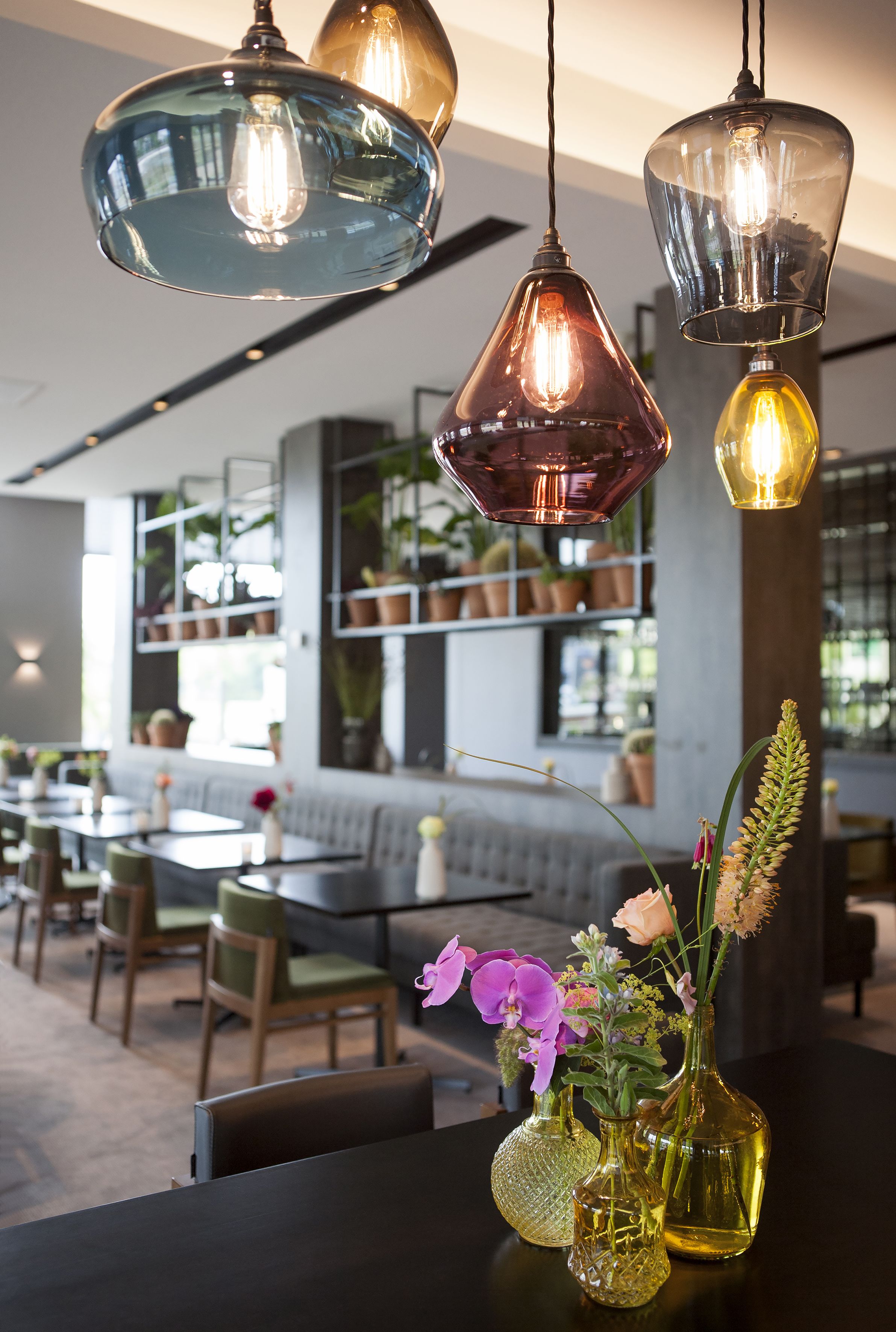 Interior de un restaurante con lámparas colgantes, un arreglo floral central y una zona de estar con mesas y sillas.