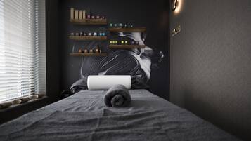 Relax in a serene space with a massage table at its center, surrounded by a striking mural and natural light.