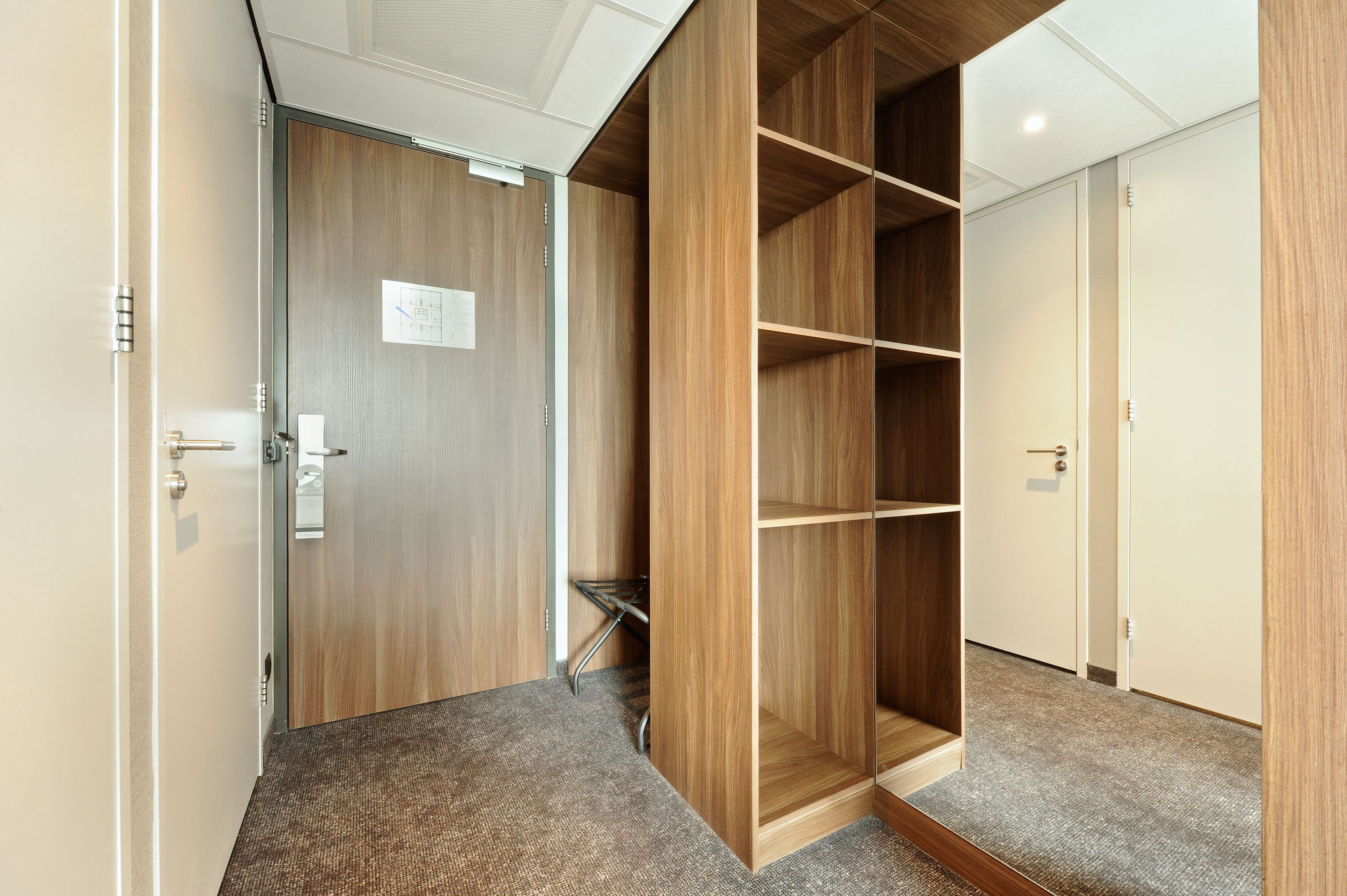 Een gang met een houten garderobe en een deur met een bordje.