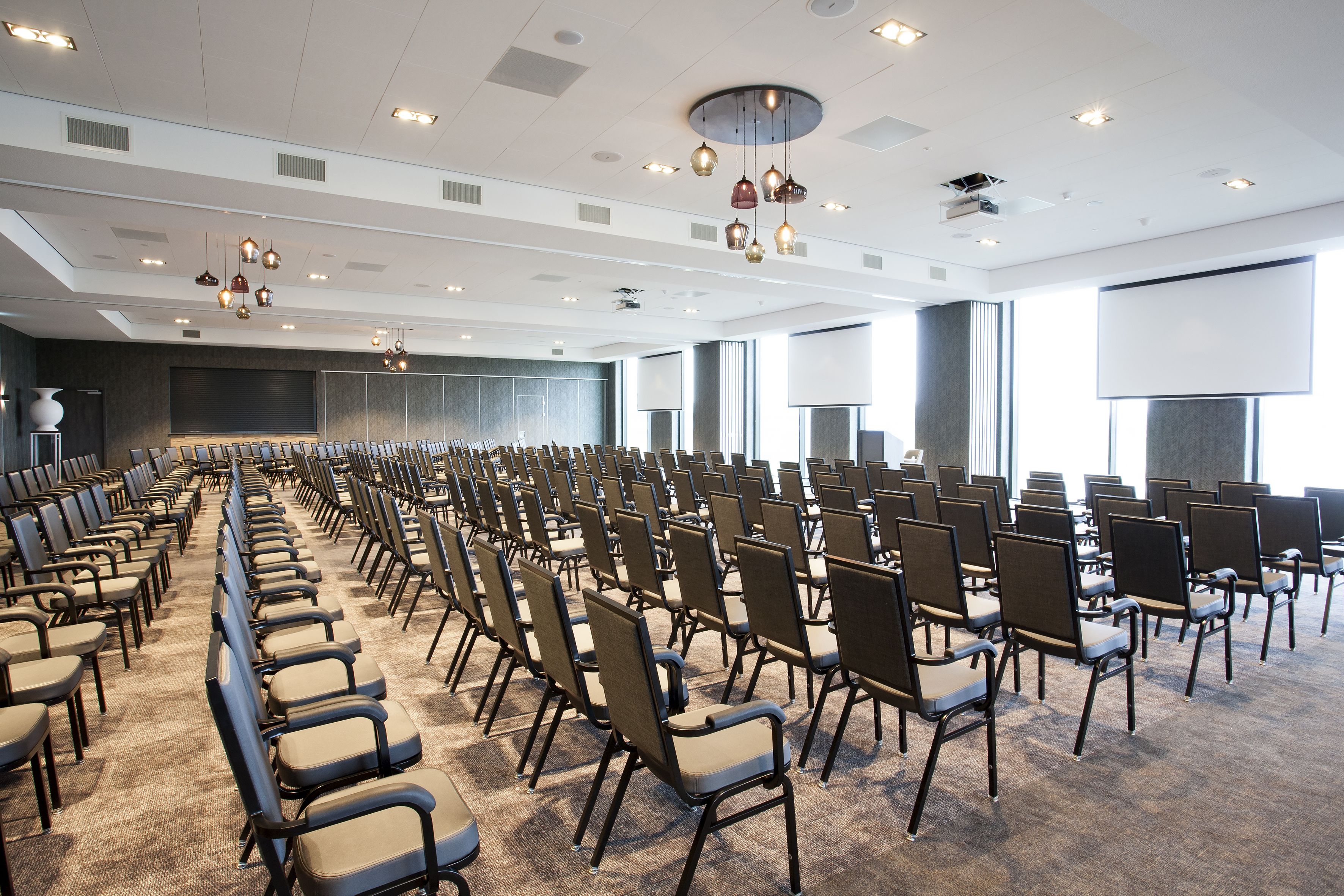 Een vergaderzaal met rijen stoelen, een groot scherm en een modern plafondontwerp.