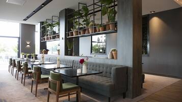 Un interior moderno con sofá, mesas de comedor, sillas y plantas en macetas.