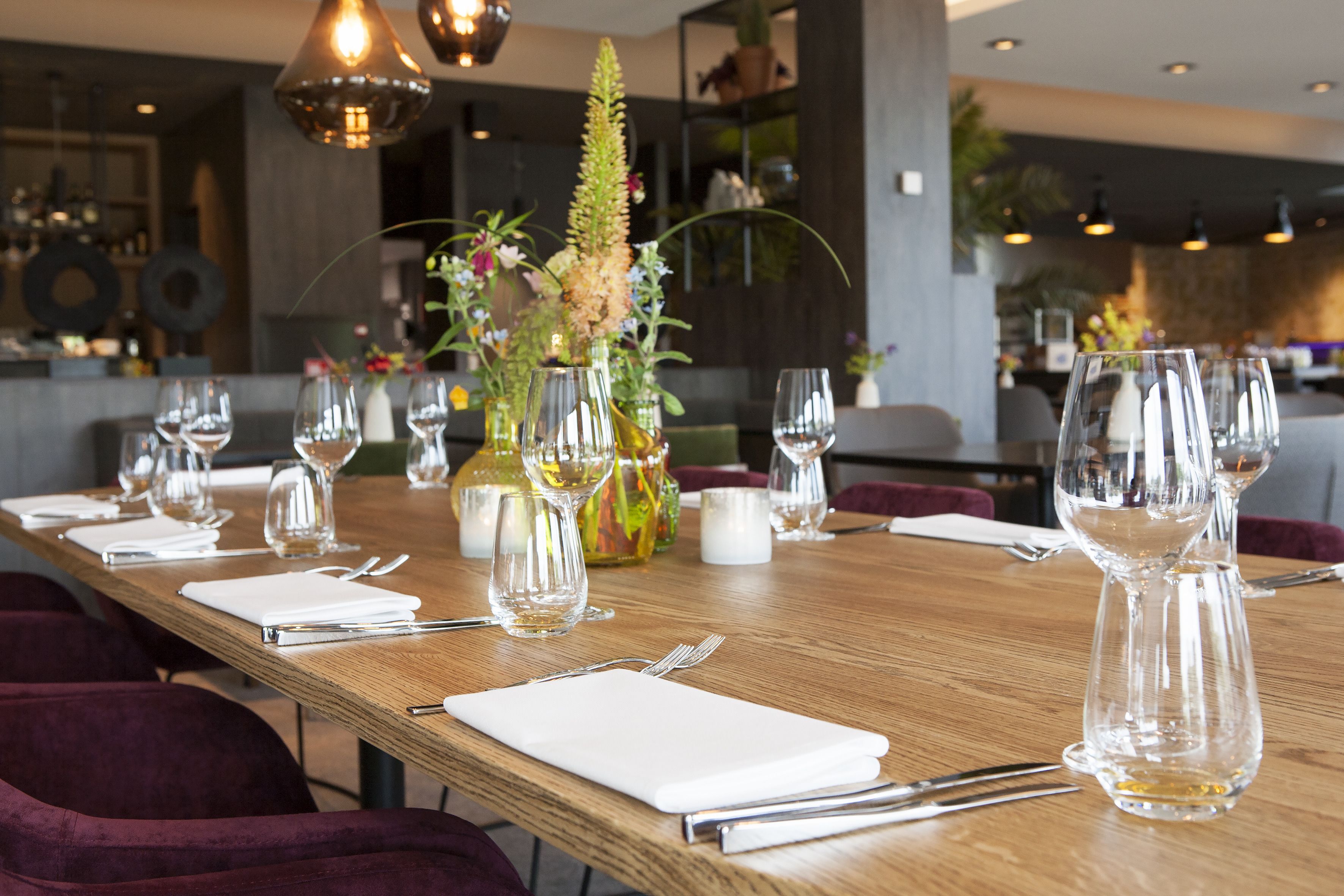 A long wooden dining table set with multiple wine glasses, cutlery, and white napkins.