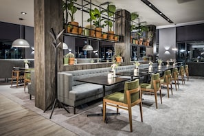 A modern dining area with a grey sofa, wooden chairs, and a long table. - Van der Valk Hotel Nijmegen - Lent (Lent)