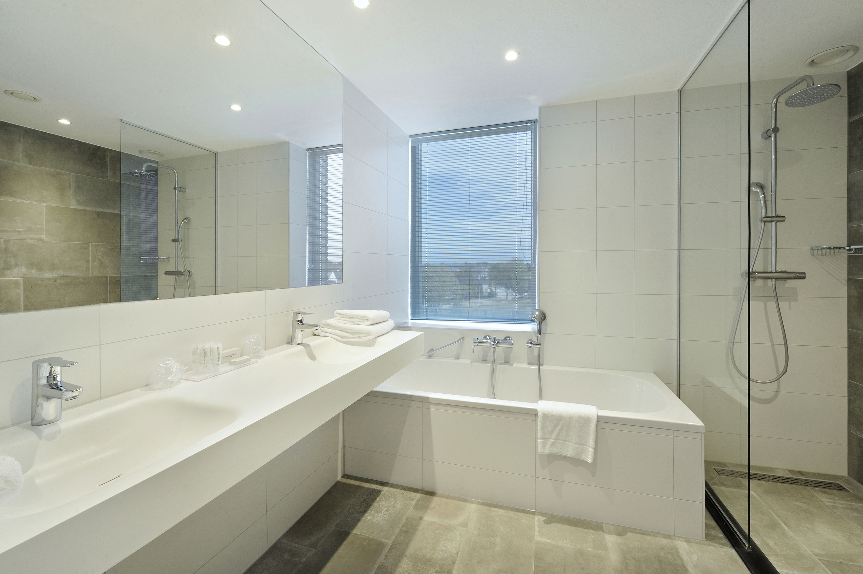 Un baño moderno con un espejo grande, dos lavamanos, una bañera y una ducha.