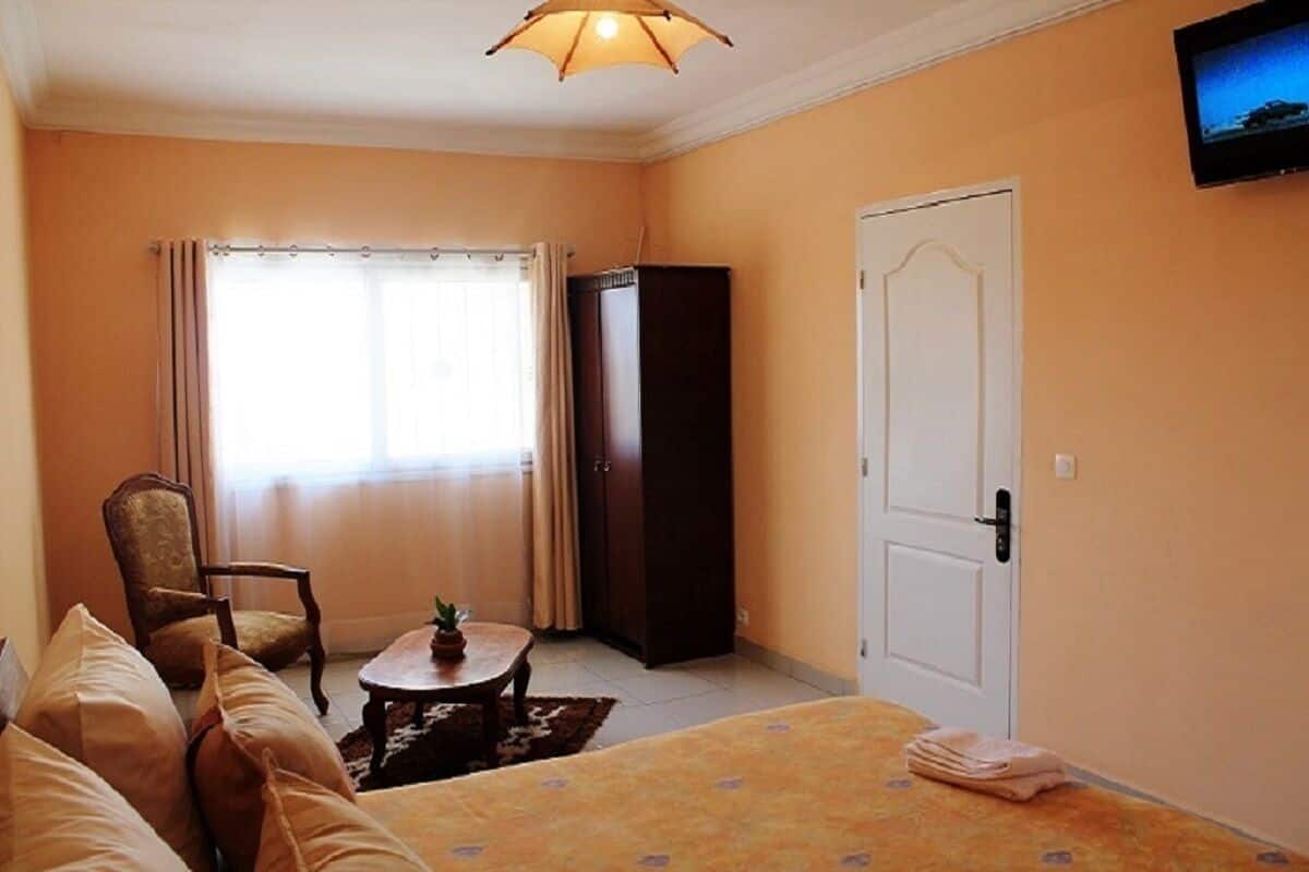 A hotel room with a bed, a chair, a small table with a plant, a wardrobe, and a television on the wall.