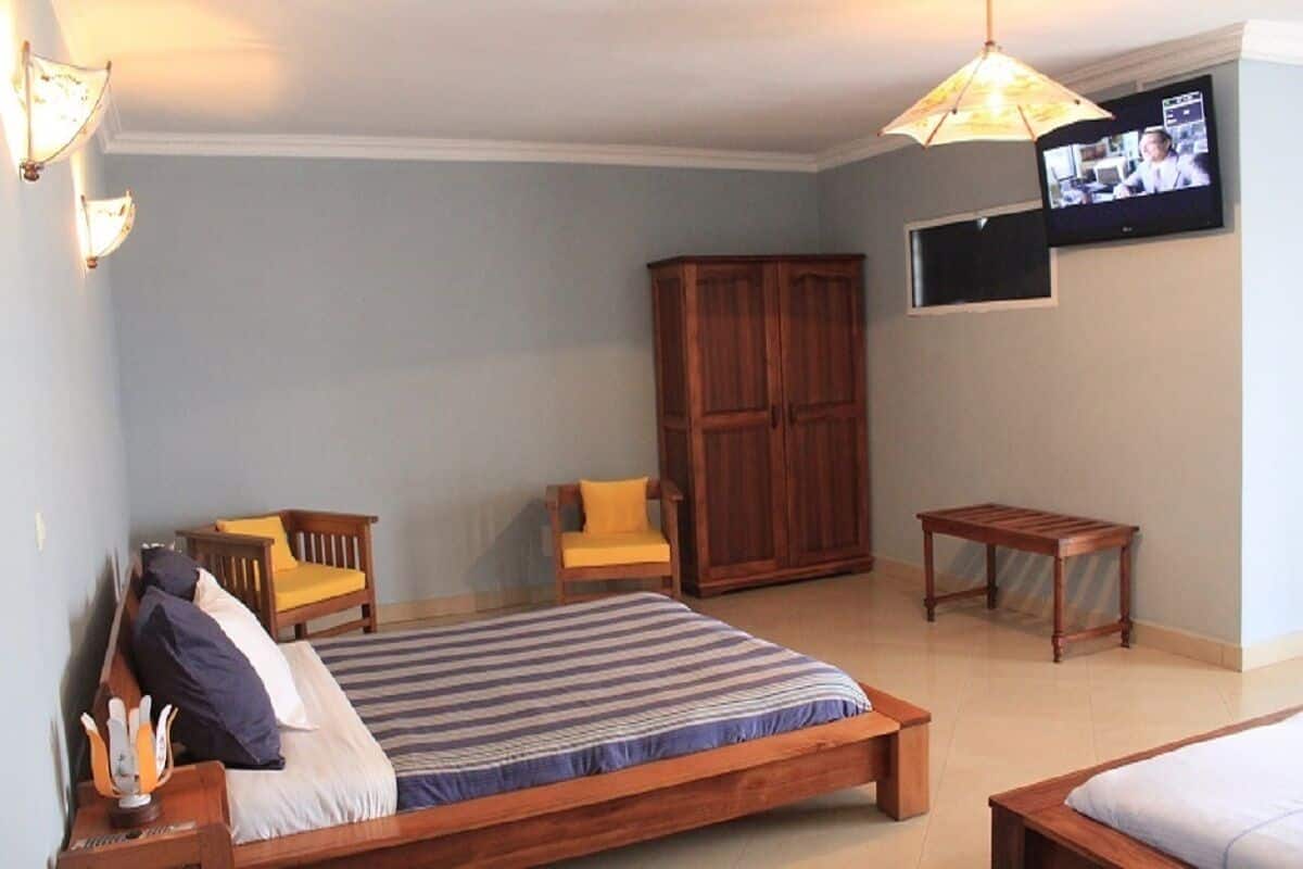 A bedroom with a bed, two chairs, a wooden cabinet, a small table, and a TV on the wall.