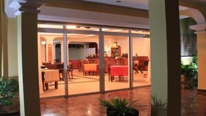 Eine geräumige Lobby mit Glastrennwand, ein Essbereich mit roten Tischen und eine Bar mit einer großen Vase.