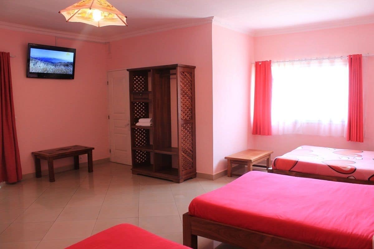 A bedroom with two beds, a TV, a wardrobe, and a window with curtains.