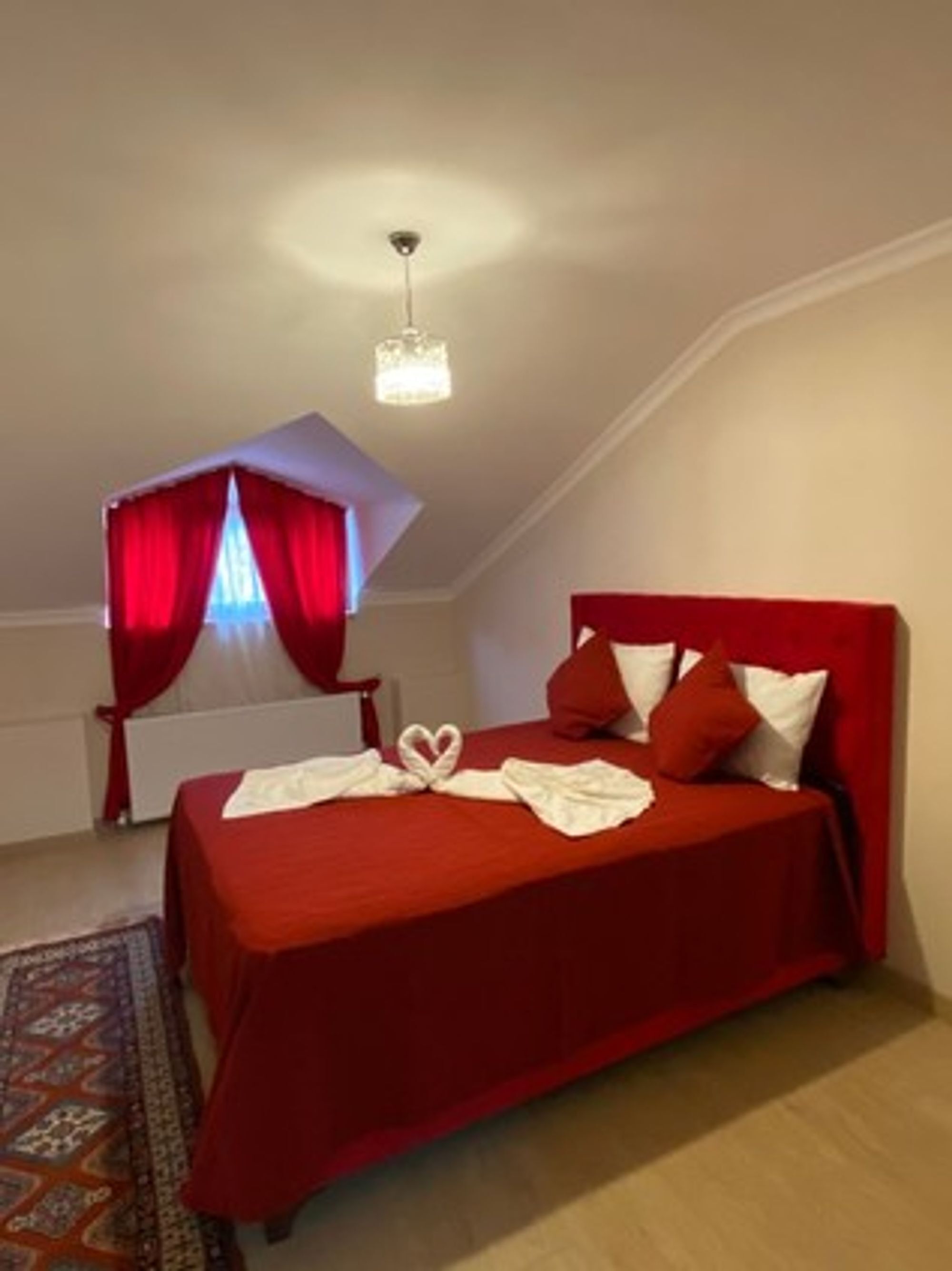 Un dormitorio con una colcha roja, una disposición de toallas en forma de corazón y un candelabro.