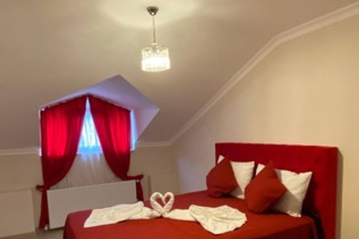Un dormitorio con una colcha roja, una disposición de toallas en forma de corazón y un candelabro.