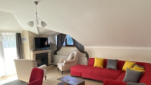A spacious living room with a red sofa, a white armchair, a red chair, a coffee table, and a flat-screen TV mounted on the wall. - Assortie La Villa Hotel (Sile)