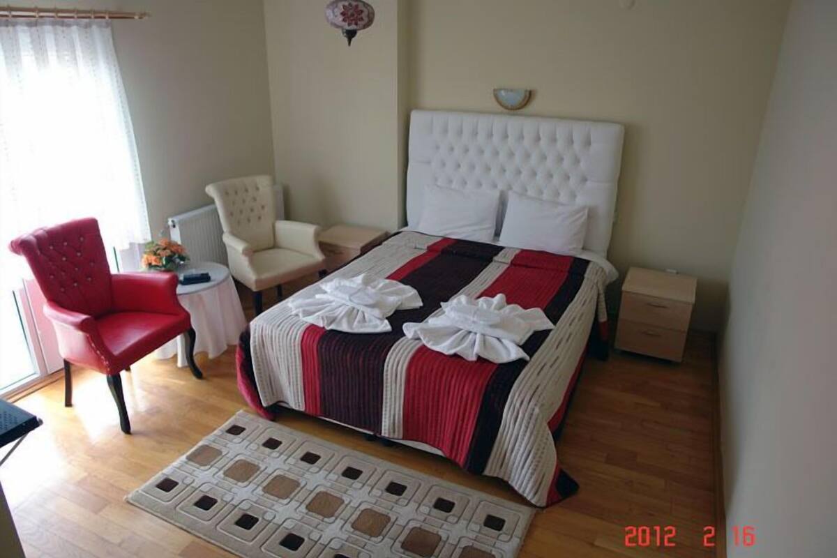 Un dormitorio ordenado con una cama, dos sillas, una mesita y una mesilla de noche.
