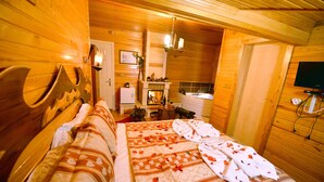 A wooden cabin bedroom with a bed, a fireplace, a television, and a small table with a lamp. - Assortie La Villa Hotel (Sile)