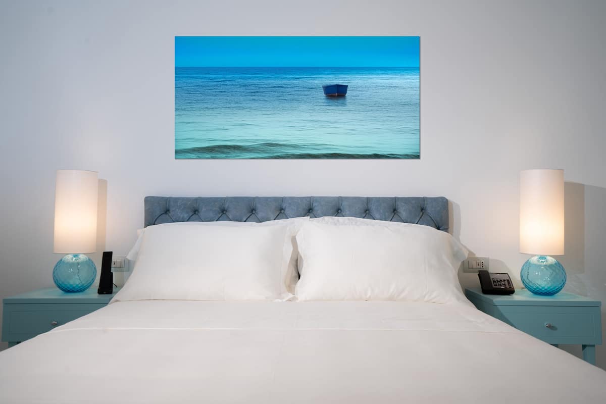 Un dormitorio con cama, dos mesitas de noche, un cuadro colgado en la pared de un barco en el agua, y dos lámparas.