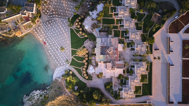 An aerial view of a coastal resort with multiple buildings, a parking lot, and a beach area.