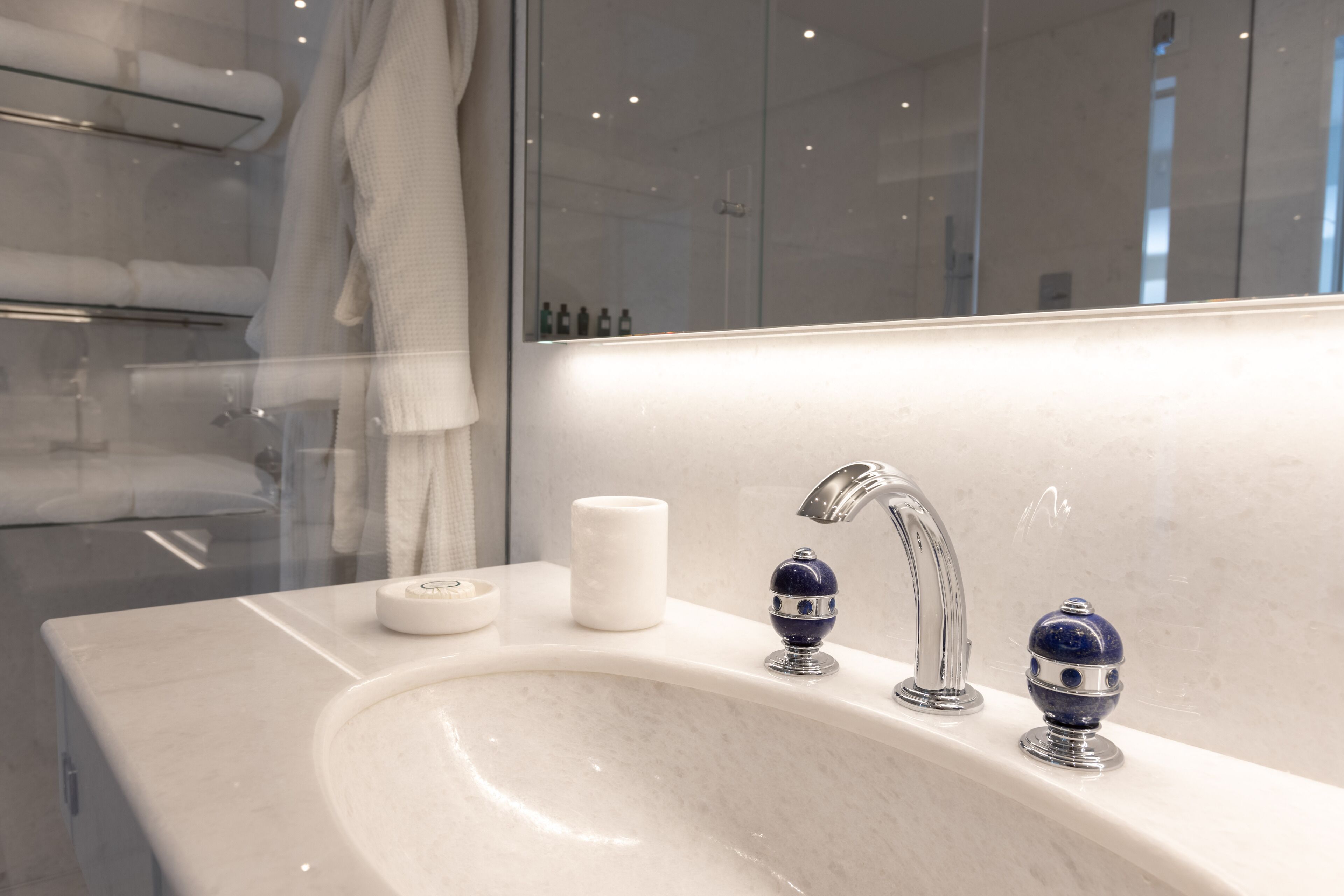 A modern bathroom with a white sink, two blue soap dispensers, a white soap dish, and a glass shower enclosure.