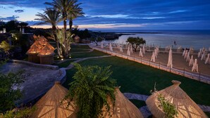 A beachside resort with thatched umbrellas, a palm tree, and a view of the sea.