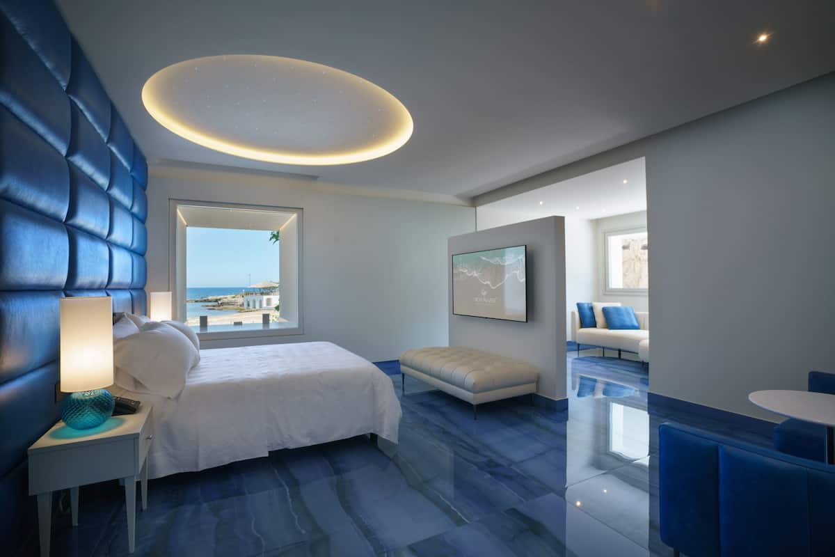 Una habitación de hotel moderna con una cama grande, un área de descanso con vistas y una mesa de comedor.